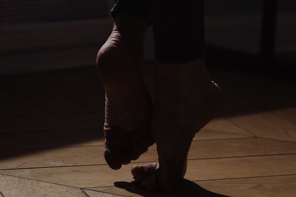 A person's feet positioned for a balanced movement on a dark floor.